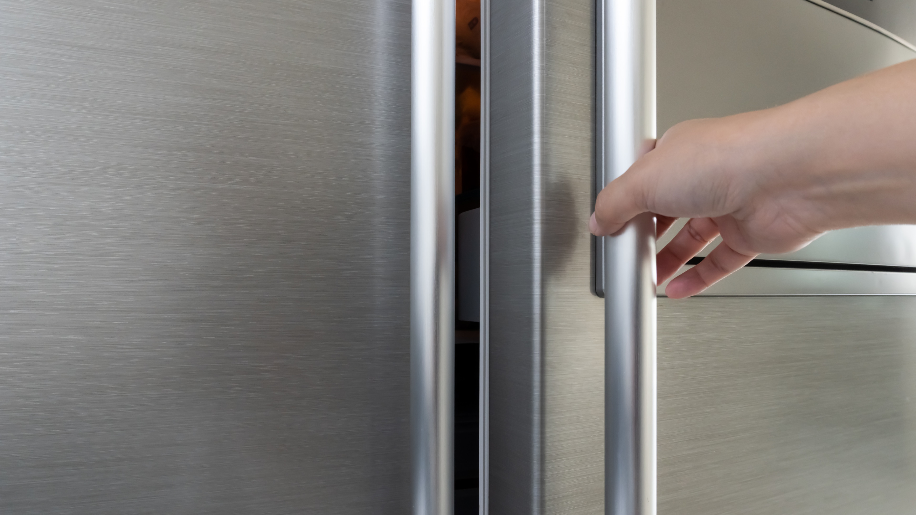 Woman's hand opening a gray metallic refrigerator door